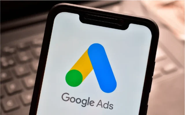 Google Ads logo displayed on a smartphone screen with a laptop keyboard in the background.